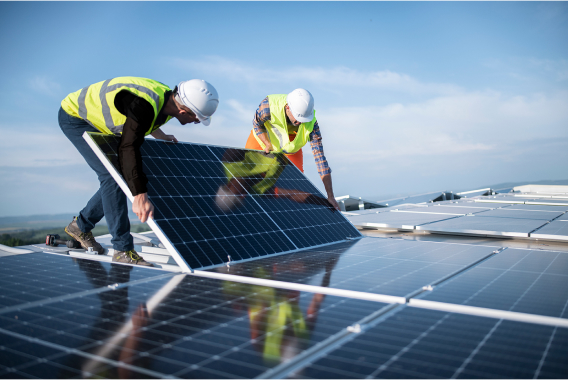 Two worker with hardhats holding solar panel on a rooftop Two worker with hardhats holding solar panel on a rooftop