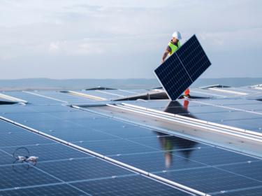 Worker with hardhat holding solar panel on a rooftop 