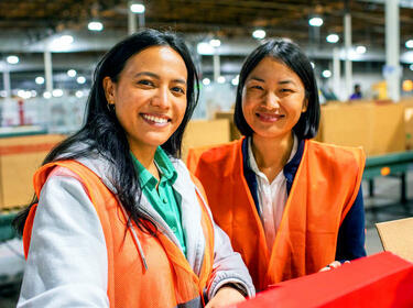 Dos mujeres sonriendo en un almacén con chalecos naranjas Dos mujeres sonriendo en un almacén con chalecos naranjas