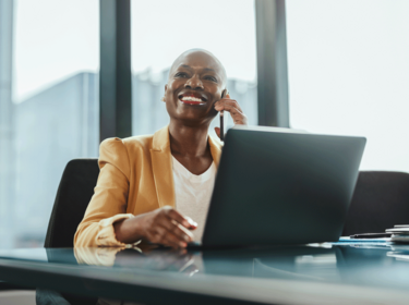 Person working on a laptop, talking on the phone and smiling